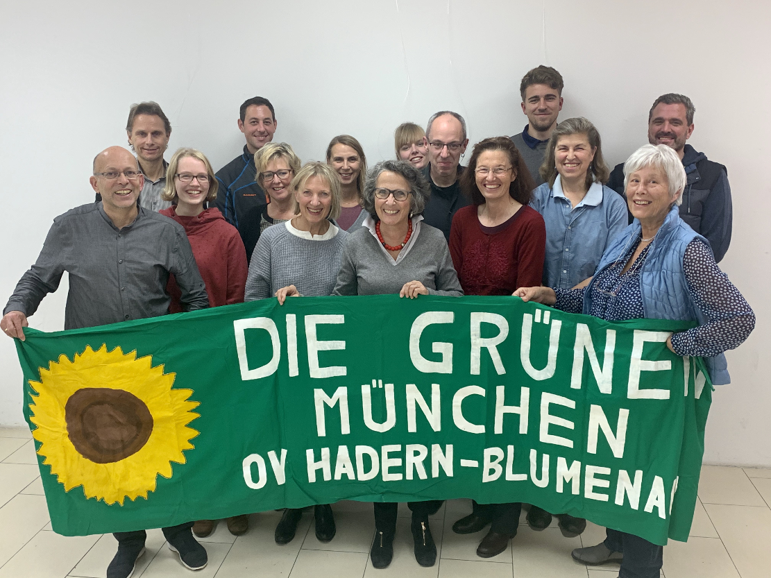 Gruppe von OV-Mitgliedern, die ein Grüns Tuch mit dem Text Die Grünen München OV Hadern-Blumenau sowie einer gemalten Sonnenblume halten.